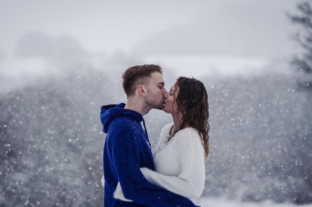 Seitliches Portrait eines Liebespaars mit nassen Haaren, das sich im Schneesturm küsst.