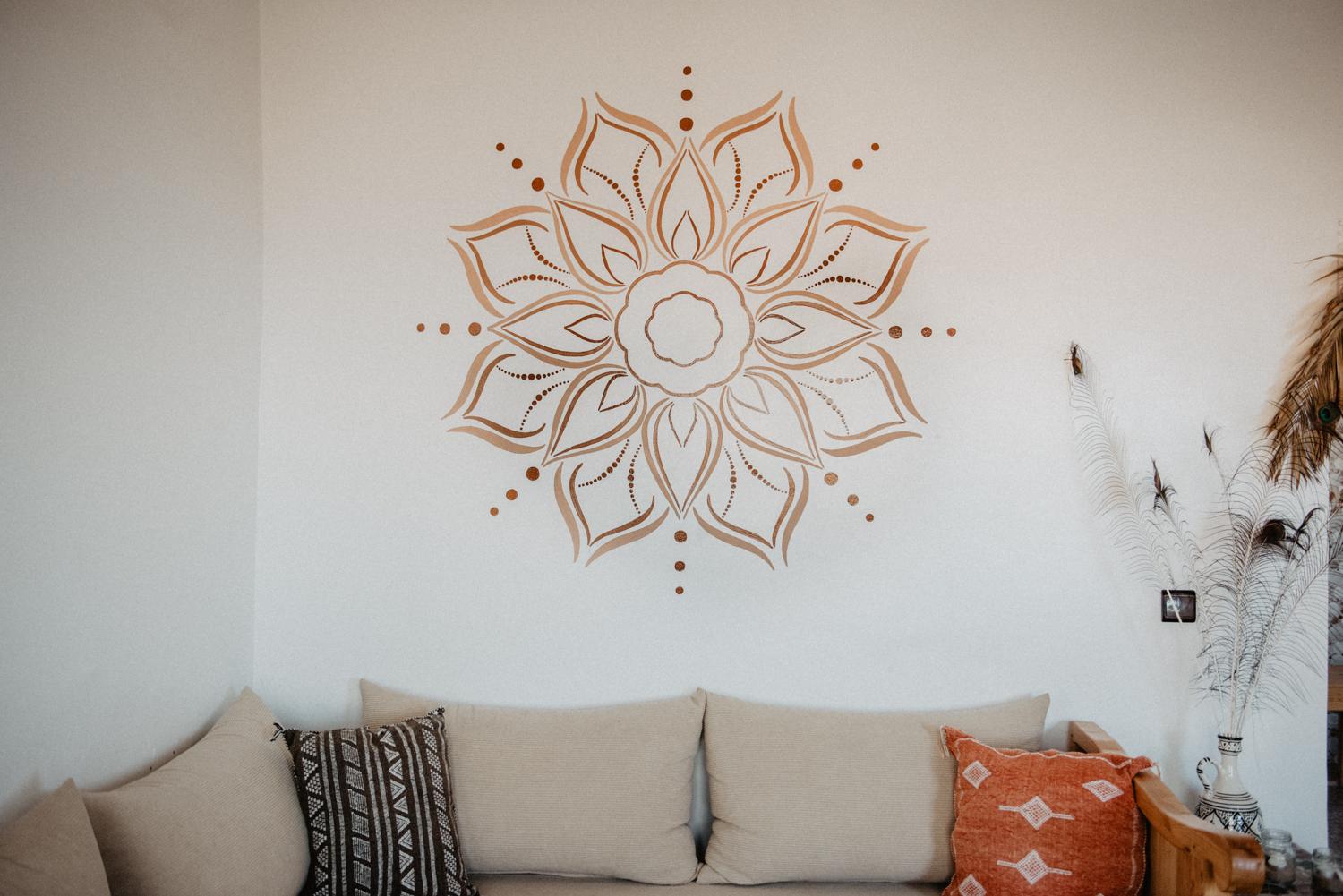 Handgemaltes Mandala in verschiedenen Brauntönen auf einer Wand über dem Sofa in einem Wohnzimmer im Boho-Stil.