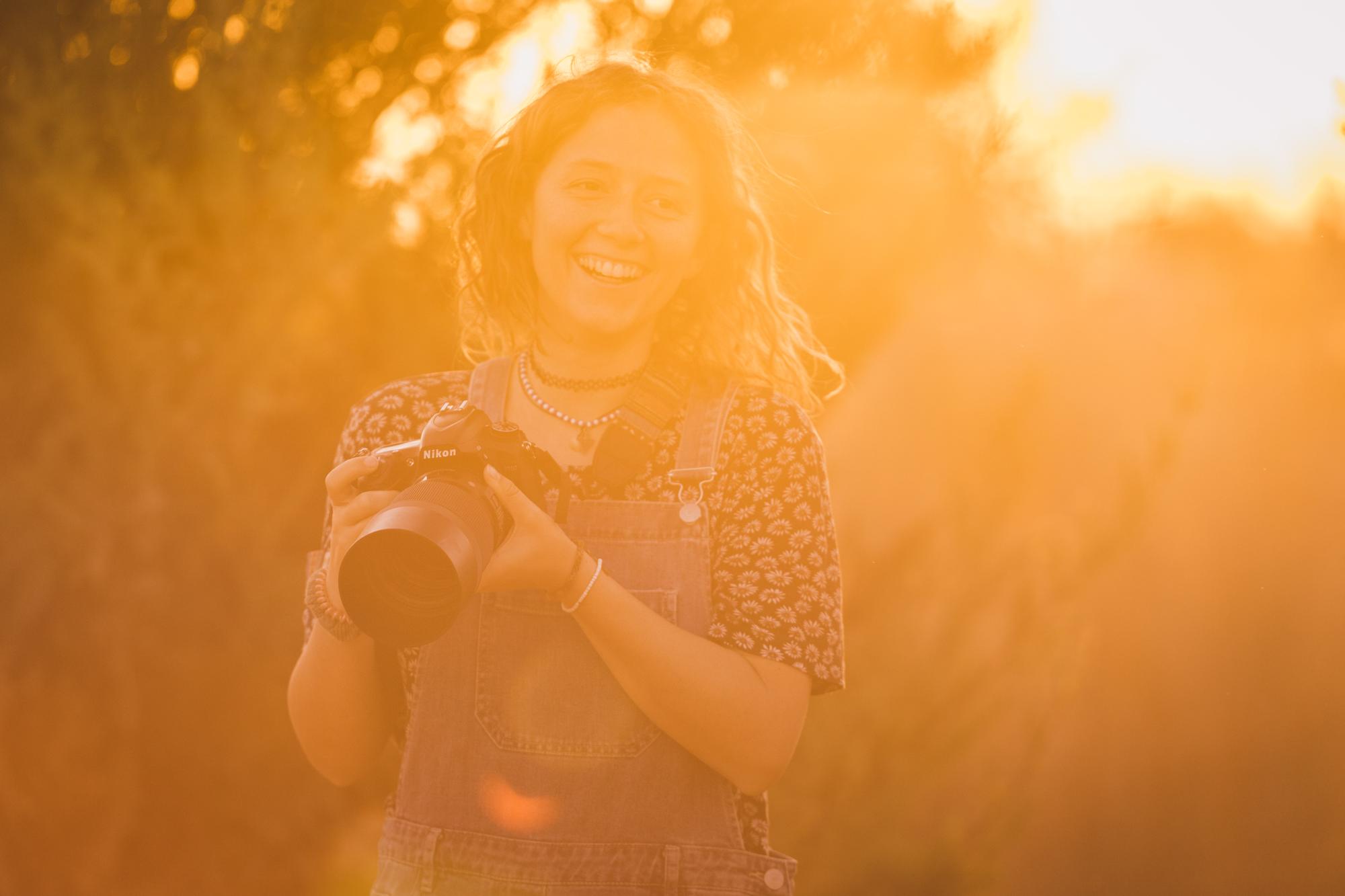 Portrait der Tierfotografin Julie Moquet mit lockigem schulterlangem Haar und ihrer Kamera in der Hand im Sonnenuntergang.