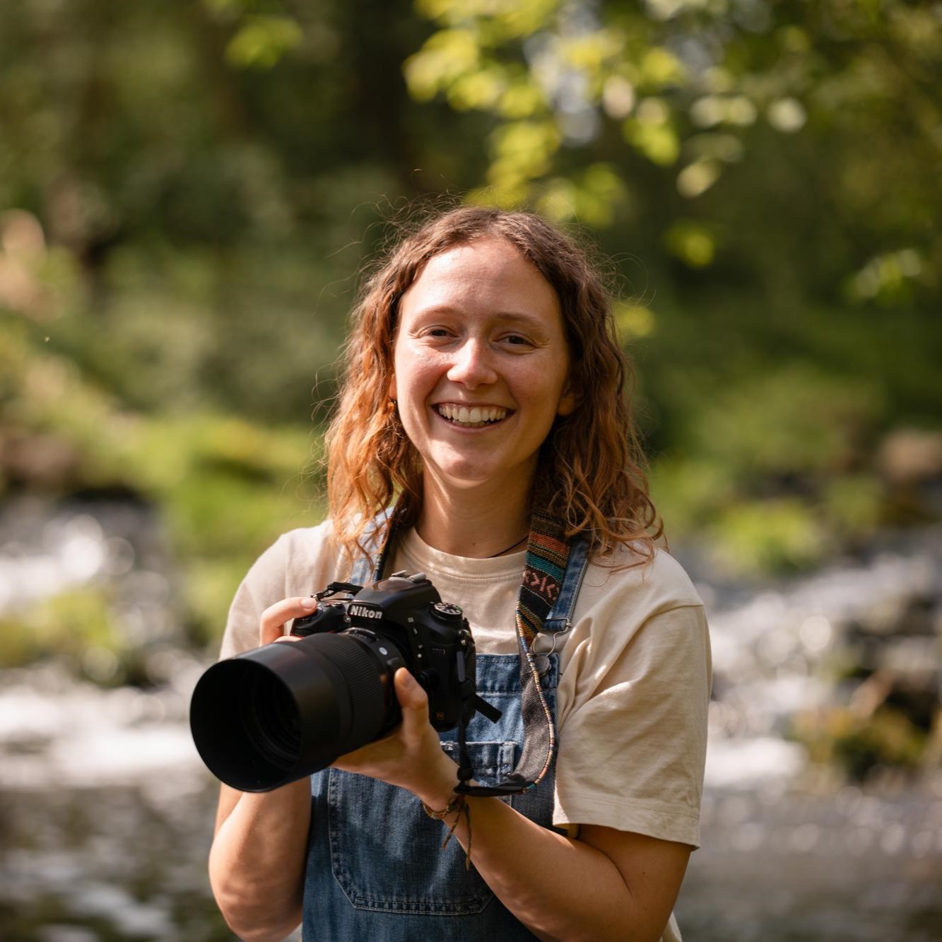 Portrait der Tierfotografin Julie Moquet mit lockigem schulterlangem Haar und ihrer Kamera in der Hand im Sonnenuntergang.