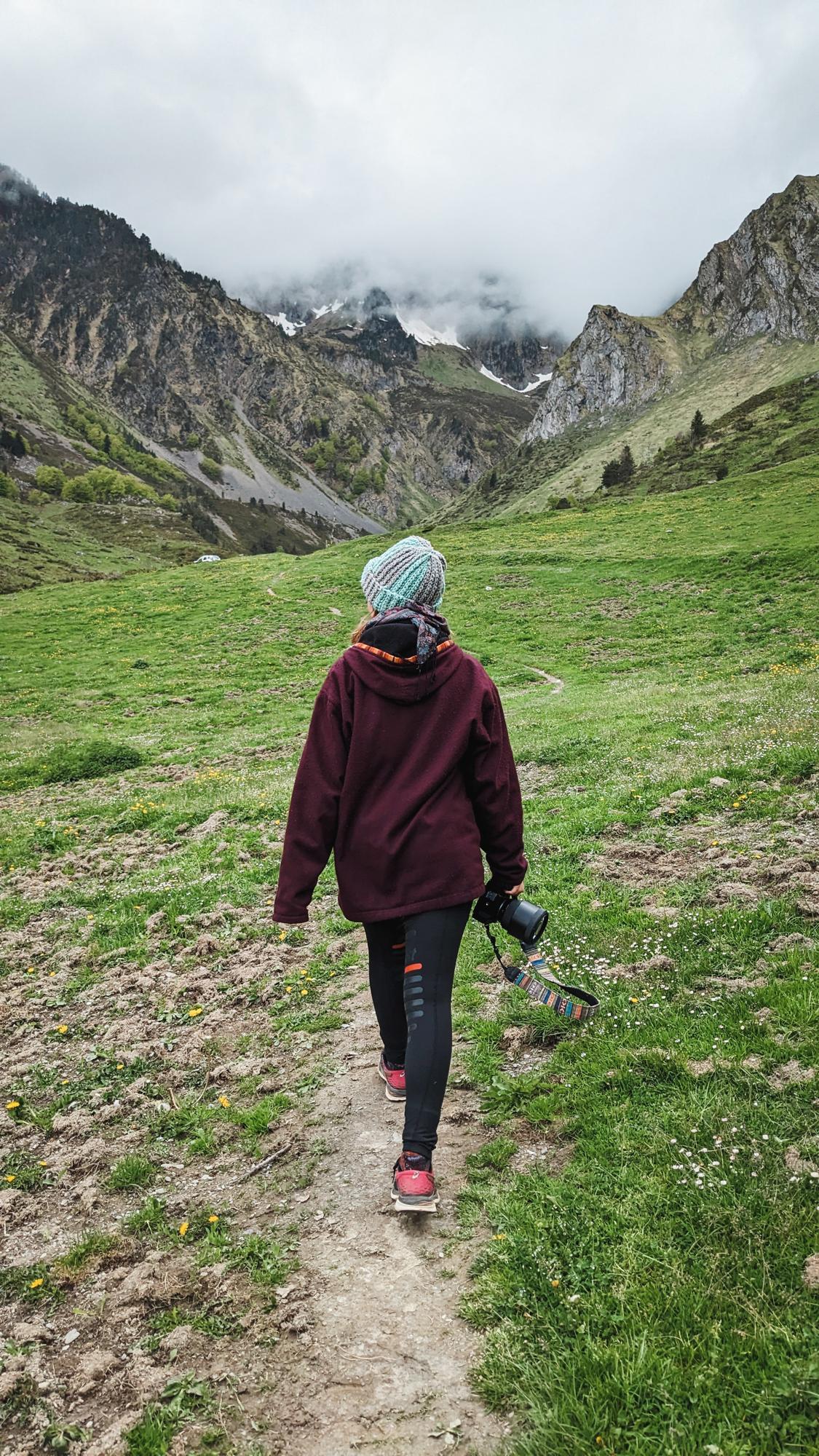 Fotografin von hinten. Auf einen Berg in den Pyrenäen zulaufend. Kamera locker in der rechten Hand zur linken Seite schauend.